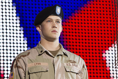 A young man in a tan U.S. Army uniform and black beret stands before a red, white, and blue patterned background.