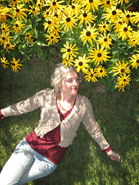 A woman in a tan cardigan and maroon shirt lies on green grass next to bright yellow black-eyed Susans.