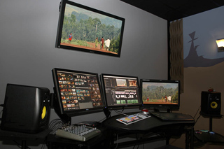 Video editing workstation with three monitors on a desk and a large screen mounted on the wall.