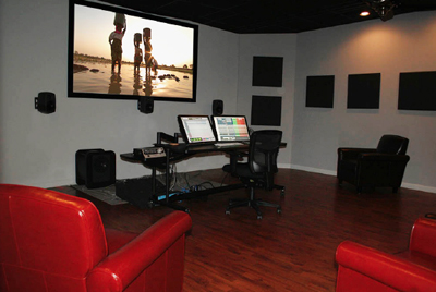 A video editing studio featuring a large projection screen, dual monitors, and red leather seating.