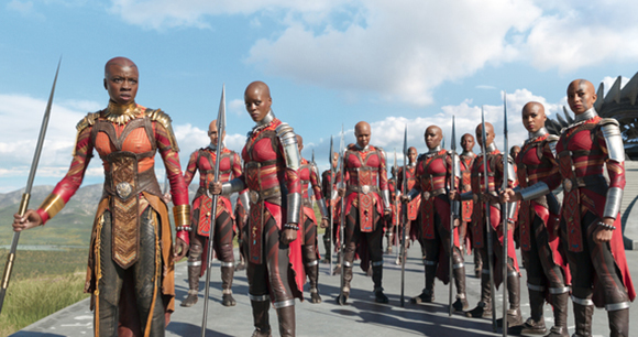 A line of female warriors in red and gold armor holding long spears under a blue sky.