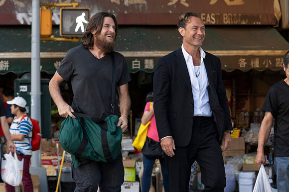 Two smiling men walk past a storefront with Chinese characters on a city street.