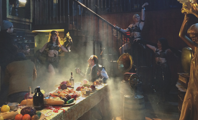 People in costume gather around a table filled with food in a smoky, dimly lit room.