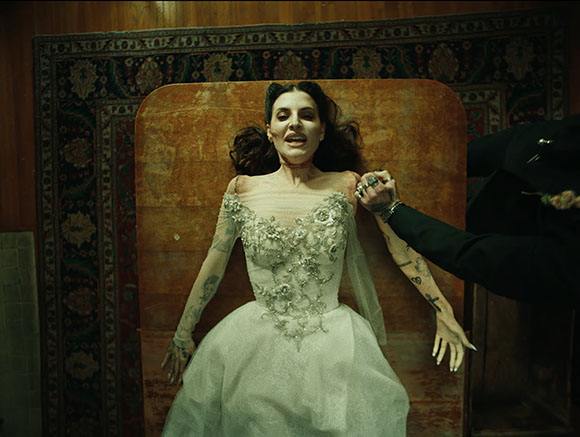 A woman in a white embellished gown lies on an orange padded surface against a patterned rug.
