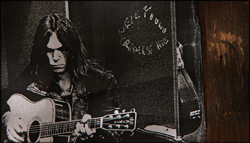 Black and white portrait of a long-haired musician playing an acoustic guitar.