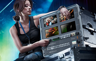 A woman in a black tank top adjusts controls on a large video production switcher.