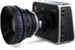 A black digital camera with a large, prominent lens positioned on a white background.