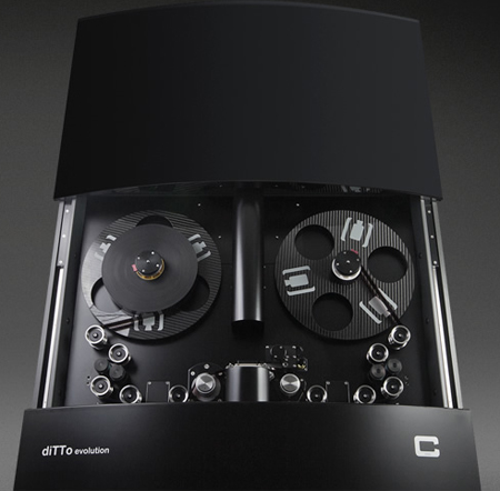 A black reel-to-reel tape recorder with two large tape reels and various control knobs.