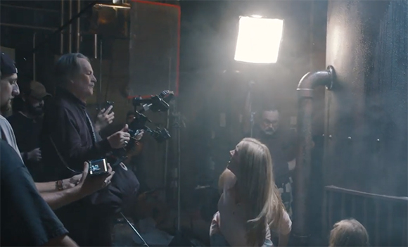 A film crew operates cameras and lights in a dark, smoky studio environment.