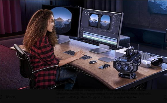 A person sits at a wooden desk with dual monitors, a keyboard, a mouse, and professional camera equipment.