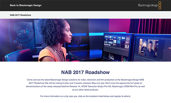 A woman with curly hair looks at two computer monitors displaying video editing software in a dark studio.