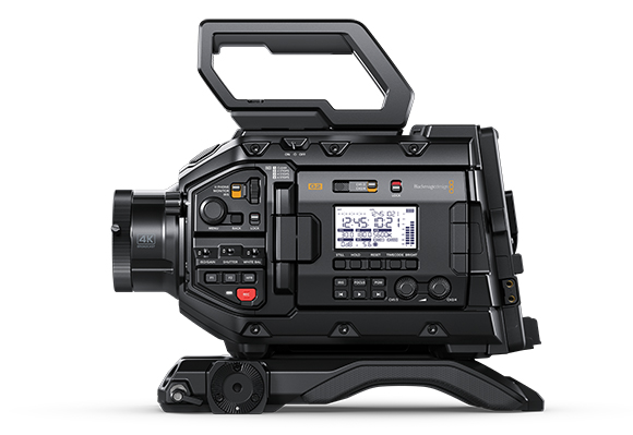 Side profile of a professional black digital video camera with various buttons, dials, and a small LCD screen.