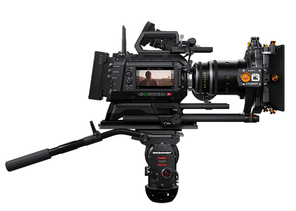 A professional black cinema camera with a large lens mounted on a heavy-duty tripod head against a white background.