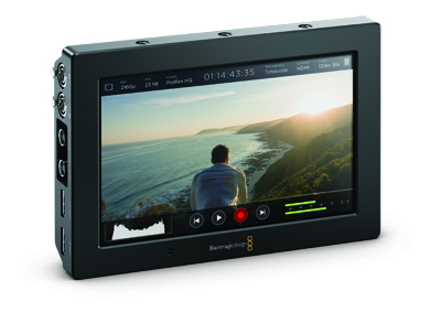 A black external video monitor displaying a man looking at a sunset over the ocean.