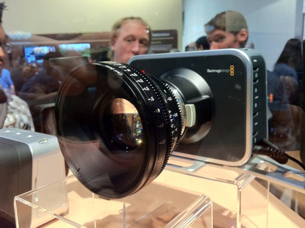 A Blackmagic Design camera with a large lens is on display, with people in the background.