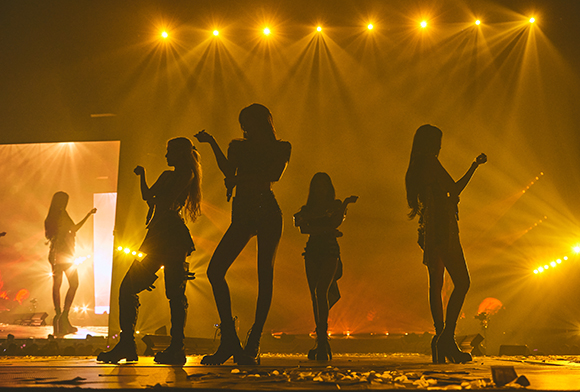 Silhouettes of five dancers performing on a stage illuminated by bright yellow spotlights.