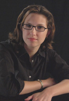 A woman with brown hair and glasses wearing a black button-down shirt against a dark background.