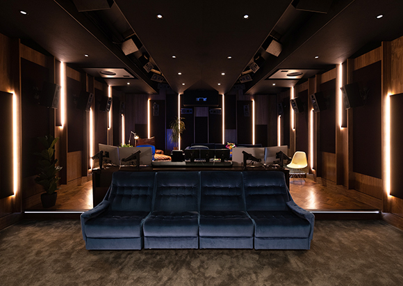 A dark, modern home theater with blue velvet seating and warm vertical light strips on wood-paneled walls.