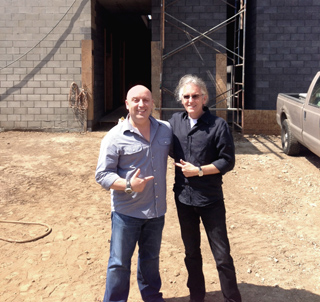 Two men posing in front of a cinder block building under construction near a pickup truck.