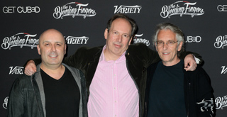 Three men standing side-by-side smiling in front of a black backdrop with white logos.