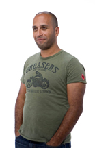 A man with short dark hair and a light beard wearing an olive green graphic t-shirt.