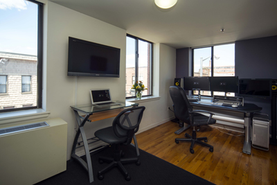 A home office featuring a glass desk with a laptop, a large monitor setup, and a wall-mounted television.