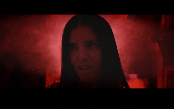 A woman with long dark hair looking forward through thick red smoke.