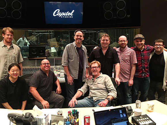 A group of nine diverse people smiling for a photo inside a recording studio with Capitol Studios logo.