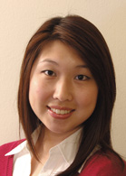A smiling woman with long brown hair wearing a white collared shirt and a red sweater.
