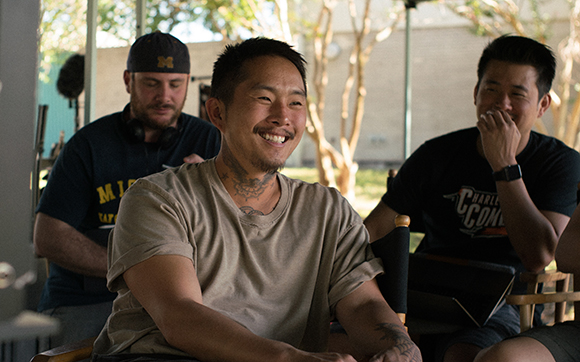 Three men sit together outdoors, smiling and laughing during a break.