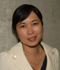 A woman with dark hair smiling while wearing a white blazer and a necklace.