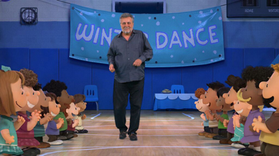A man walks through two rows of smiling animated children in a gym decorated with a Winter Dance banner.