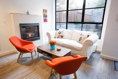 A living room featuring a white sofa, two orange armchairs, a coffee table, and a fireplace near a large window.