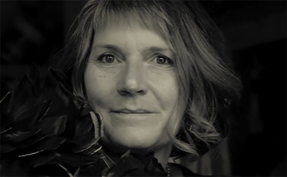 Black and white close-up portrait of a woman with light-colored hair and bangs looking at the camera.