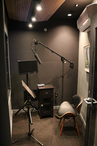 A small recording studio with a microphone on a boom arm, a music stand, and a chair.