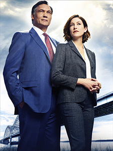 A man in a blue suit and a woman in a grey suit stand together against a cloudy sky.