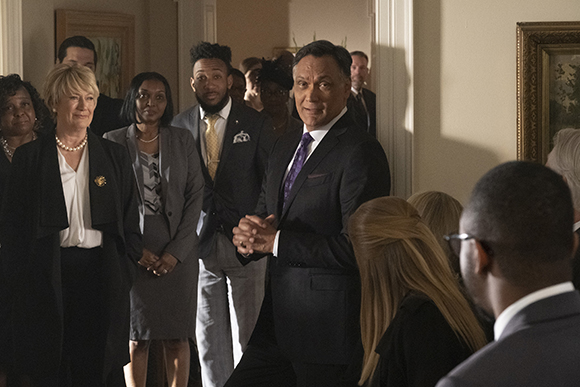 A group of diverse people in business attire standing in a brightly lit indoor hallway.