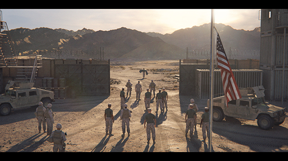 Soldiers walk through a fenced desert outpost toward mountains under a bright sun.