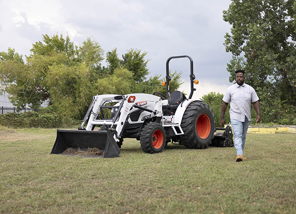 A man walks past a white tractor with a front loader in a grassy field.