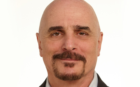 A bald man with brown eyes, a dark mustache, and a goatee looking directly at the camera.