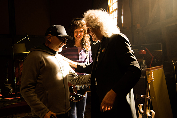Three people stand together in a dark studio illuminated by a bright light source.
