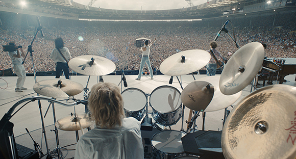 View from a stage behind drums and cymbals looking out at a large crowd in a stadium.