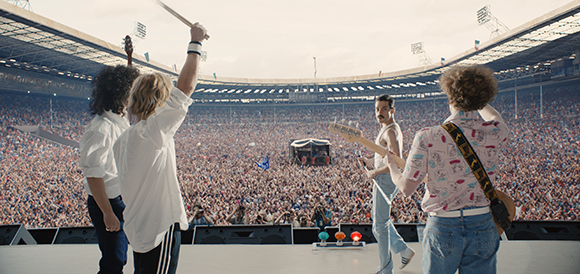 Musicians on a stage performing for a large crowd in a massive outdoor stadium.
