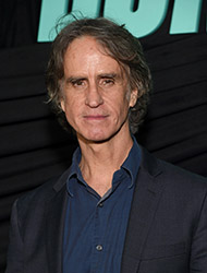 A man with wavy graying hair wearing a dark blazer over a blue button-down shirt.