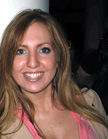 A smiling woman with long blonde hair wearing a pink top and tan jacket.