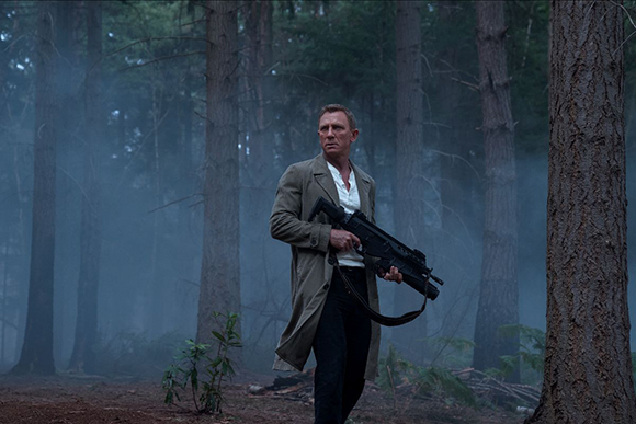 A man in a light trench coat holds a black rifle while walking through a foggy, wooded area.