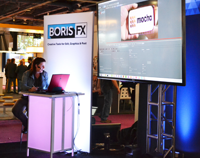 A woman sits at a high table using a laptop next to a large monitor displaying Mocha software.