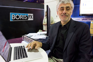 A man in a dark blazer sits at a desk with a laptop in front of a Boris FX sign.