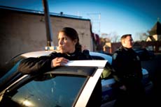 Two police officers stand near a patrol car during the day under a clear blue sky.