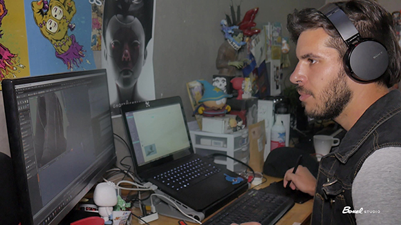 A man with a beard and headphones looks at a computer monitor while working at a desk.